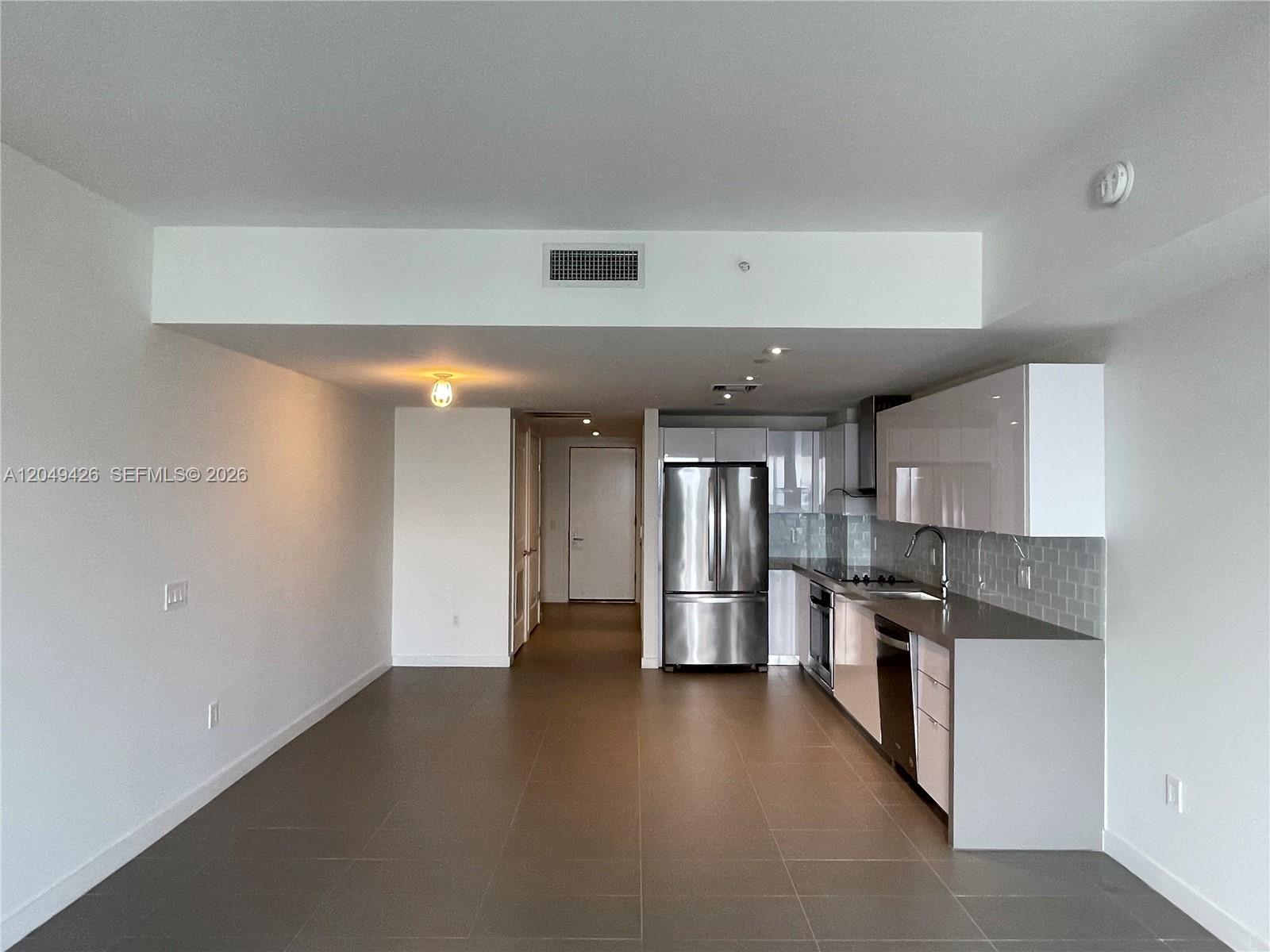 An open-concept kitchen with stainless steel appliances and white cabinetry sits beside a living area — 1600 NE 1st Ave # 3603, Miami FL 33132, MIAMI, FL