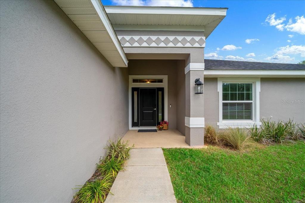 A concrete walkway leads to the covered entryway of a gray house with a black door — 97 DOGWOOD DRIVE LOOP, OCALA, FL