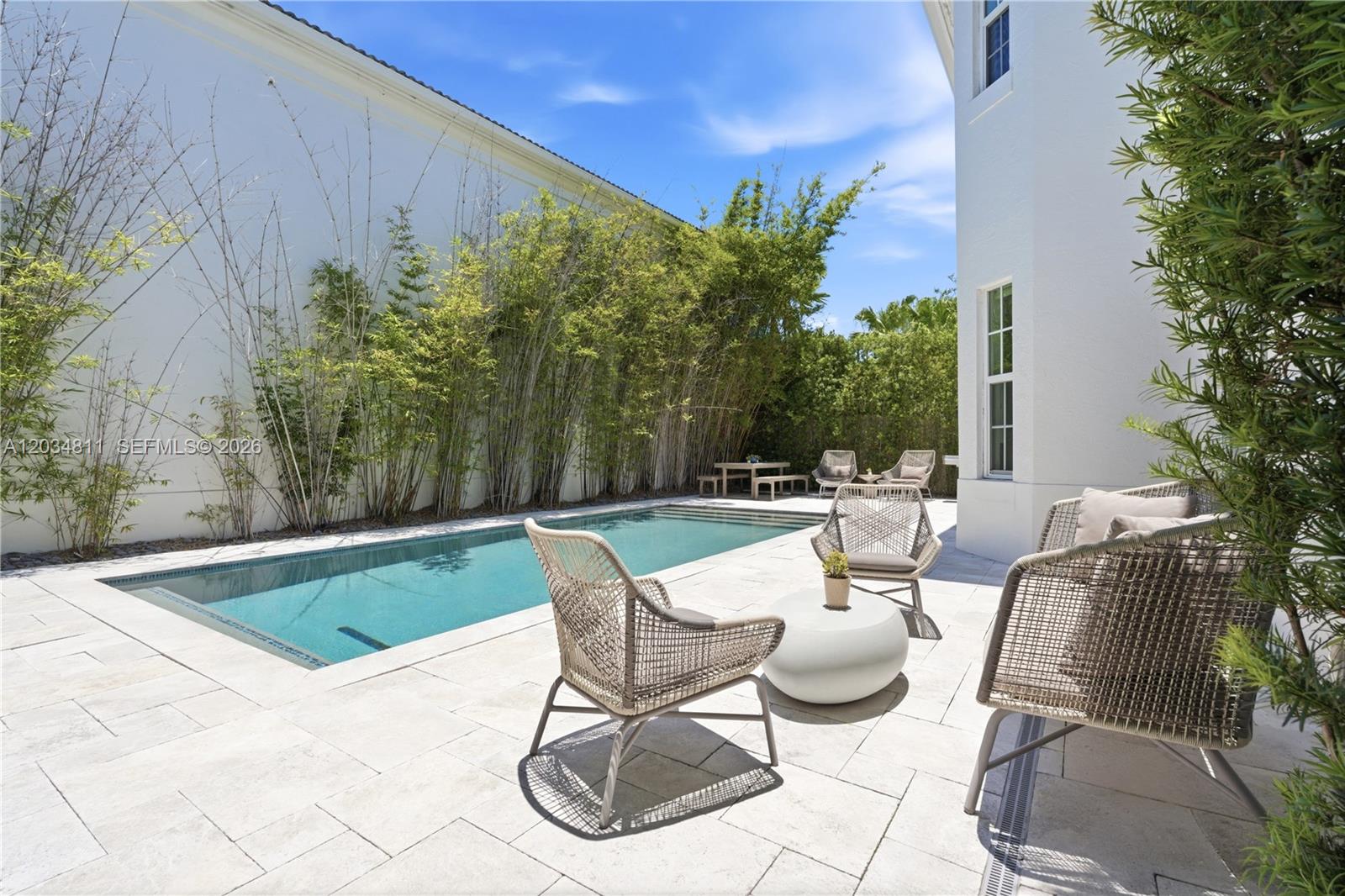 A rectangular swimming pool sits on a stone patio beside a white house with bamboo — 19941 NE 36th Pl, Aventura FL 33180, AVENTURA, FL