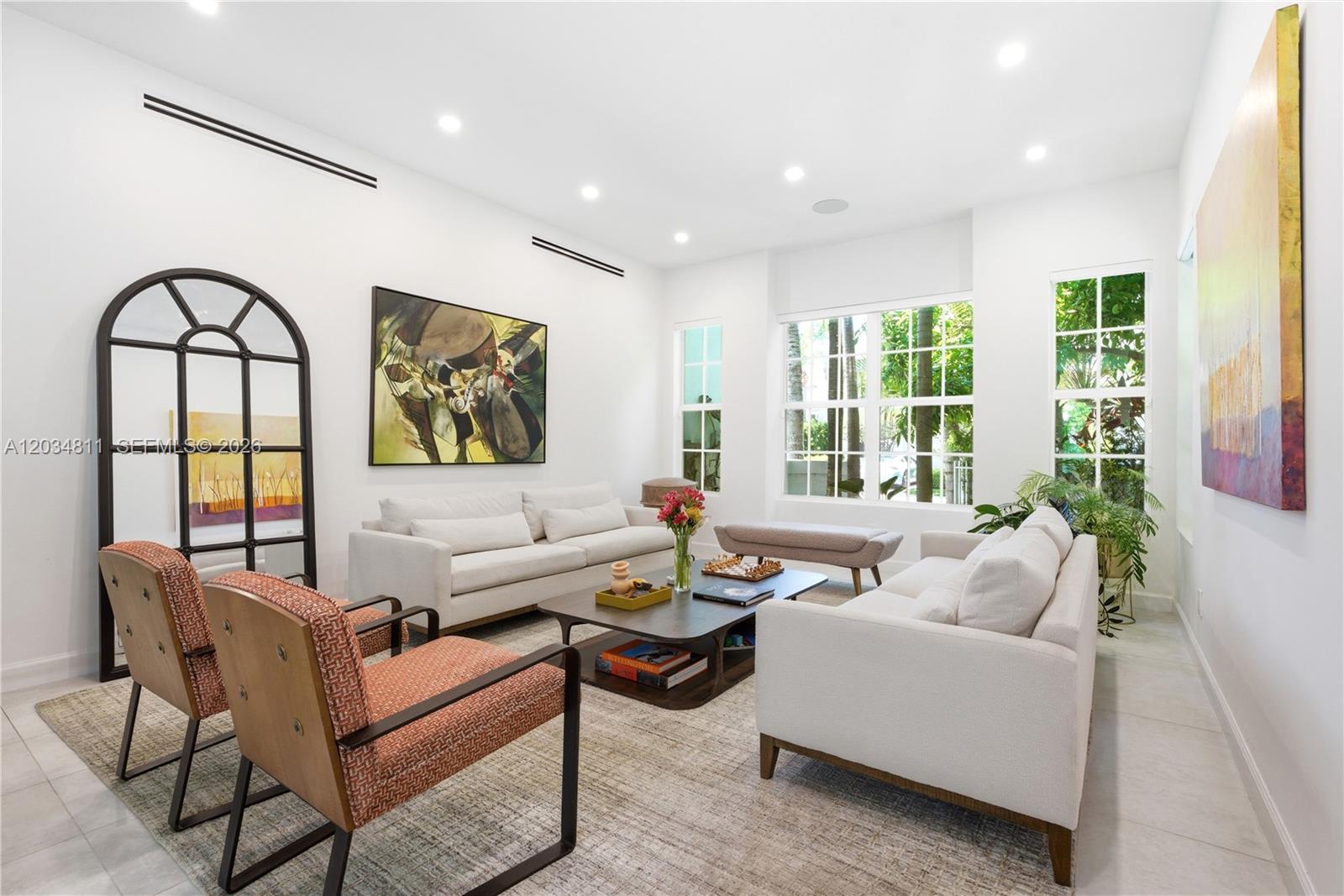 A bright living room features two white sofas, orange patterned armchairs, and a large mirror — 19941 NE 36th Pl, Aventura FL 33180, AVENTURA, FL