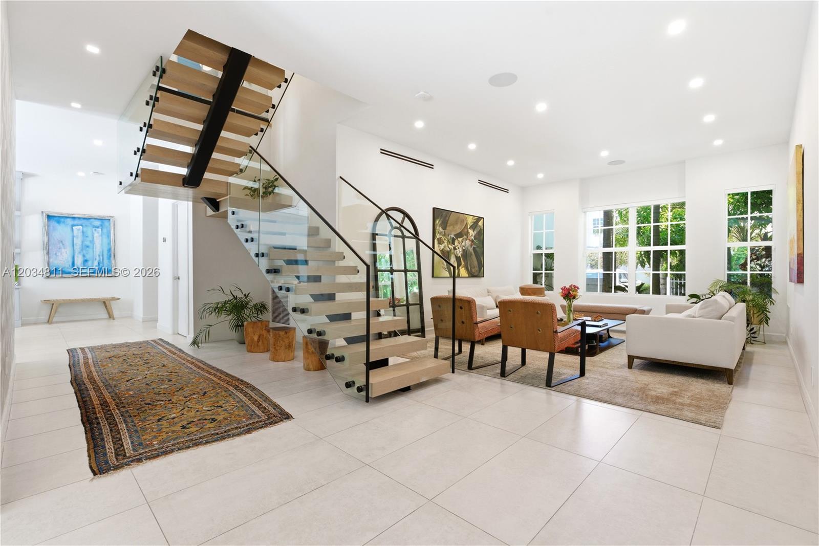 A modern living room features a floating staircase with glass railings and light tile flooring — 19941 NE 36th Pl, Aventura FL 33180, AVENTURA, FL