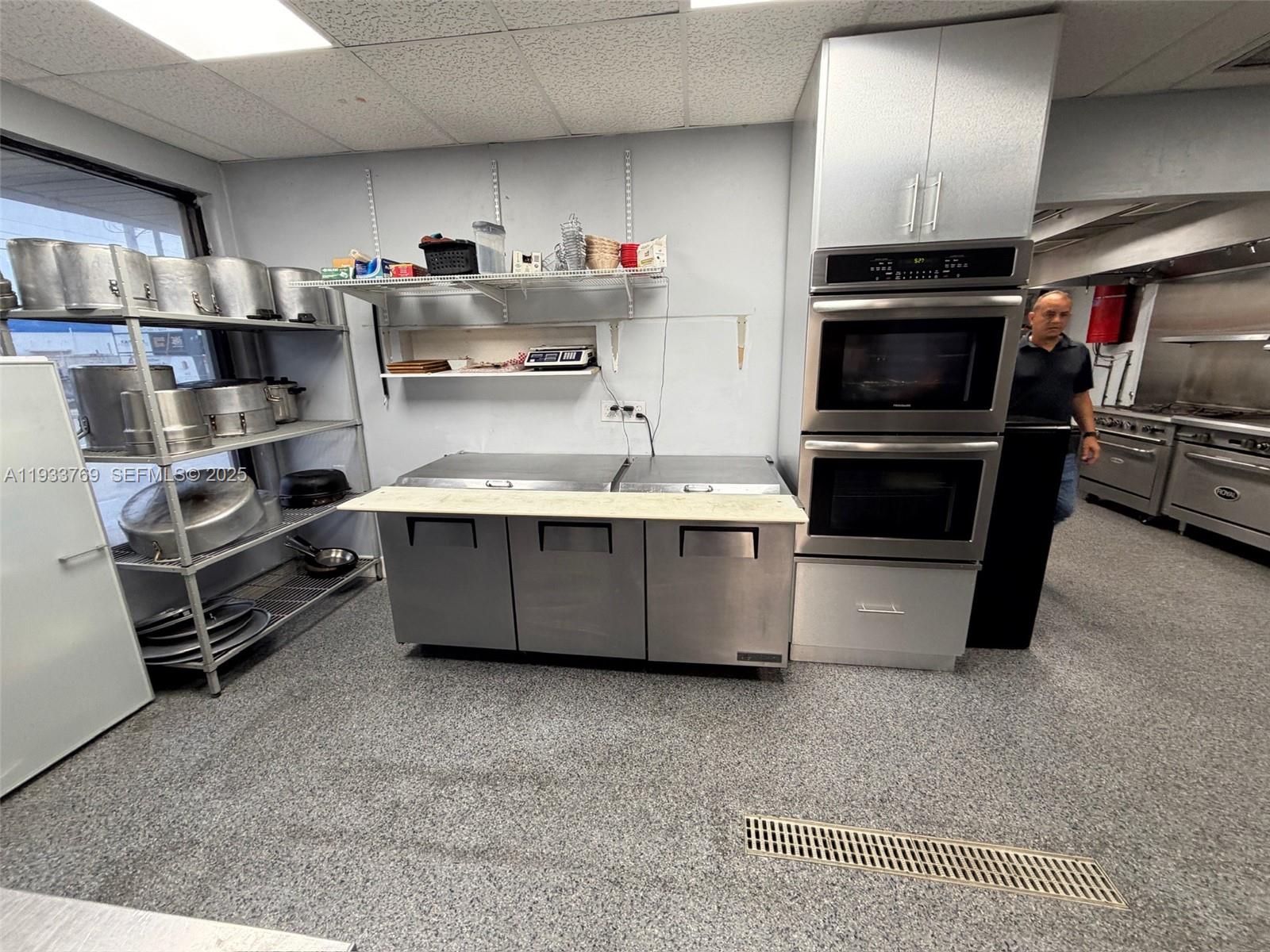 A commercial kitchen features stainless steel appliances, metal shelving, and a gray speckled floor — for sale SW restaurant, Miami FL 33166, MIAMI, FL