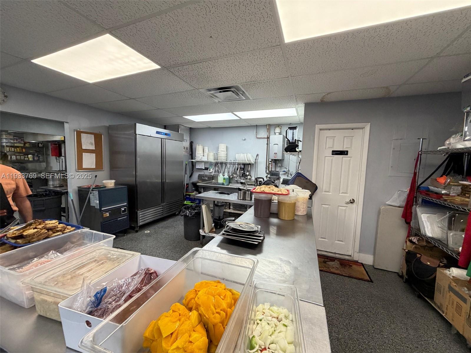 A commercial kitchen features stainless steel prep tables, a large refrigerator, and various food containers — for sale SW restaurant, Miami FL 33166, MIAMI, FL