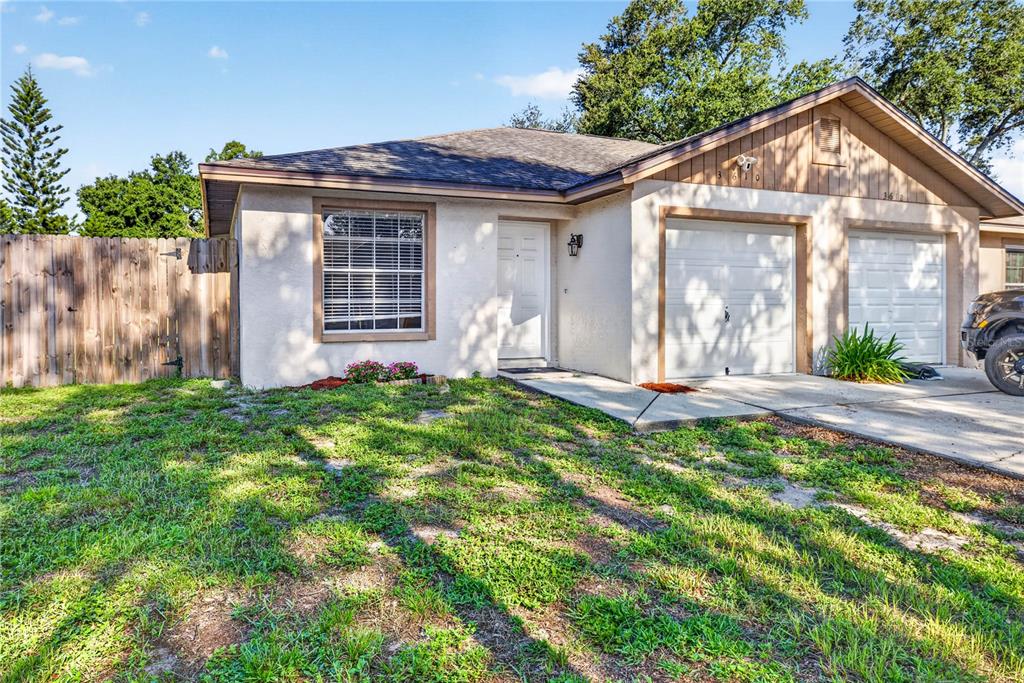A single-story house with a white stucco exterior, two garage doors, and a wooden fence — 3610 SAMMY COURT, PALM HARBOR, FL