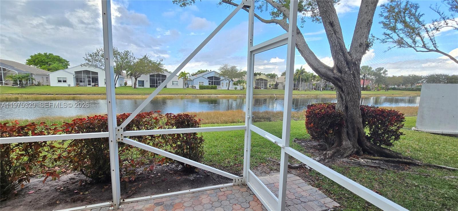 A view of a lake and neighboring houses from a screened-in patio — 8214 Bellafiore Way, Boynton Beach FL 33472, BOYNTON BEACH, FL