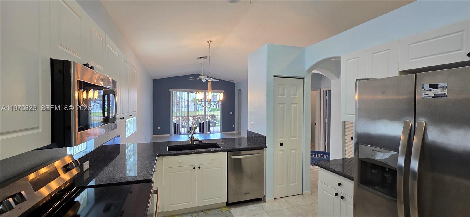 A kitchen with white cabinets, dark granite countertops, and stainless steel appliances overlooks a living area — 8214 Bellafiore Way, Boynton Beach FL 33472, BOYNTON BEACH, FL
