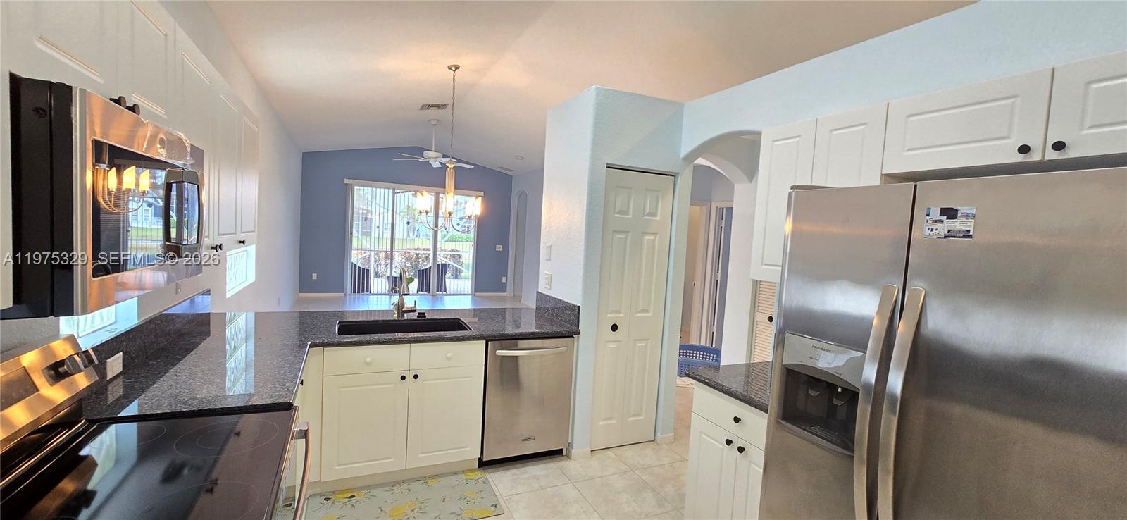 A kitchen with white cabinets, granite countertops, and stainless steel appliances overlooks a living area — 8214 Bellafiore Way, Boynton Beach FL 33472, BOYNTON BEACH, FL