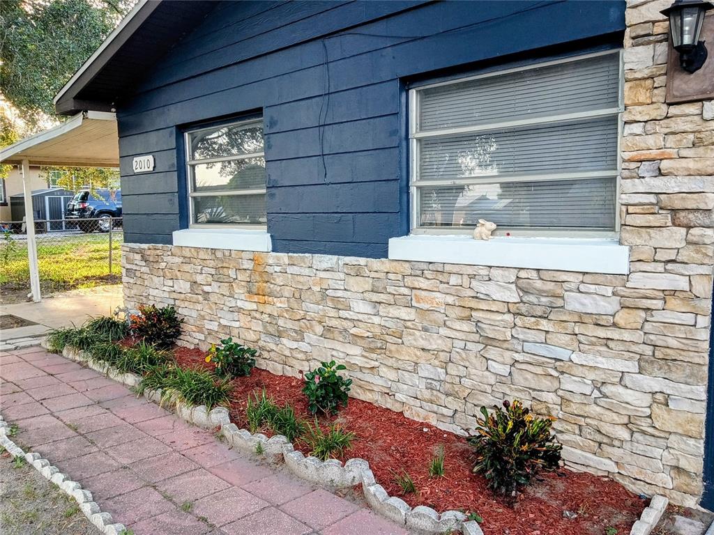 A house exterior features blue horizontal siding, a stone veneer base, and a landscaped bed — 2010 PINE AVENUE, HAINES CITY, FL