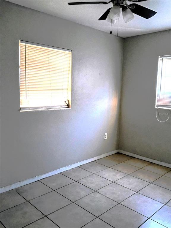 An empty room features light gray walls, tiled flooring, two windows with blinds, and a ceiling fan — 2010 PINE AVENUE, HAINES CITY, FL
