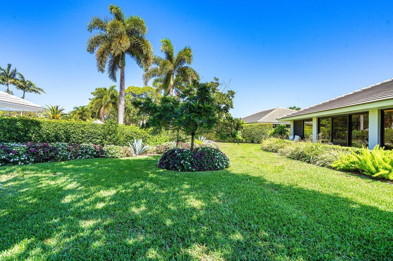 A grassy backyard features a manicured lawn, palm trees, and a house with large windows — 3661 Royal Tern Circle, Boynton Beach FL 33436, BOYNTON BEACH, FL