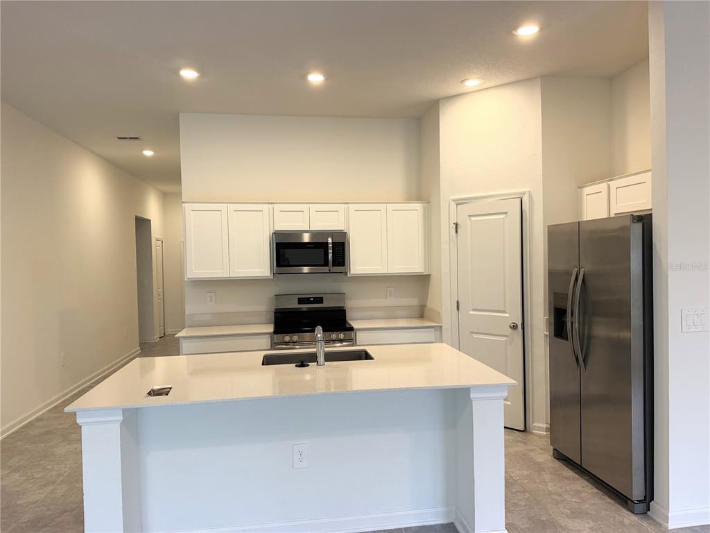 A kitchen features white cabinets, stainless steel appliances, a center island, and light-colored countertops — 1708 TEAGAN LANE, WINTER HAVEN, FL
