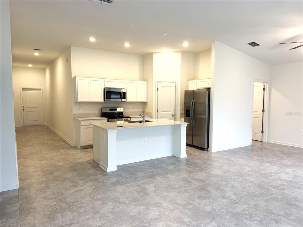 A kitchen features white cabinets, stainless steel appliances, a center island, and gray tile flooring — 1708 TEAGAN LANE, WINTER HAVEN, FL