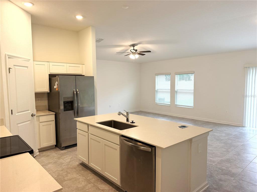 A kitchen with white cabinets, stainless steel appliances, and an island overlooks an open living area — 1708 TEAGAN LANE, WINTER HAVEN, FL