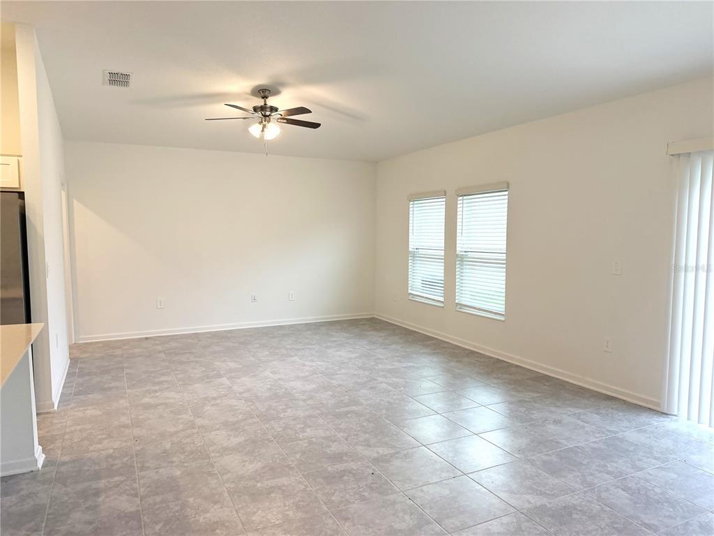 An empty room with light gray tile flooring, white walls, a ceiling fan, and windows — 1708 TEAGAN LANE, WINTER HAVEN, FL