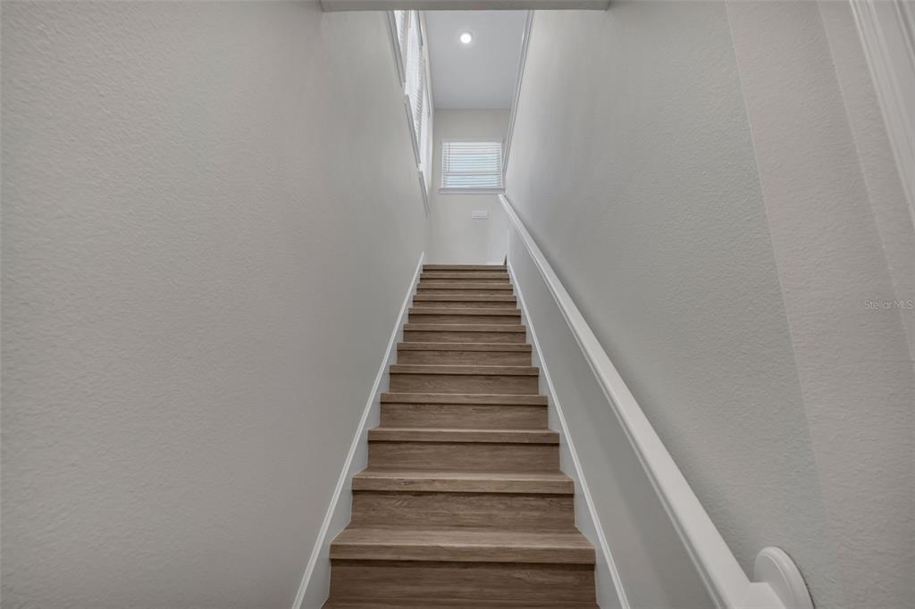 A straight staircase with wood-look treads and white walls leads to a landing with windows — 13770 ROSBASH ALLEY, ORLANDO, FL