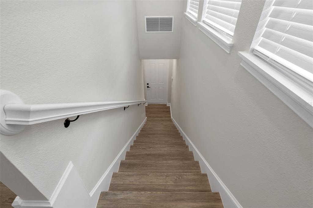 A view looking down a wooden staircase with a white handrail toward a closed door — 13770 ROSBASH ALLEY, ORLANDO, FL
