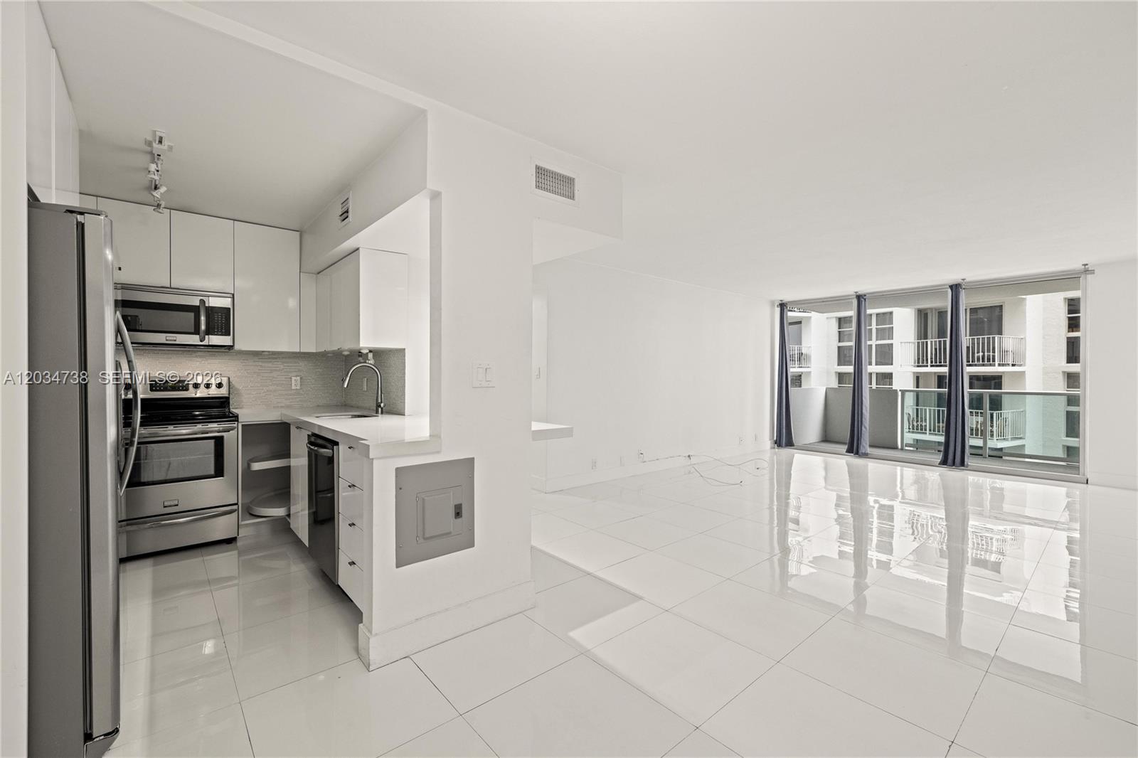 A modern kitchen with stainless steel appliances opens into a bright, tiled living area — 1200 West Ave # 622, Miami Beach FL 33139, MIAMI BEACH, FL