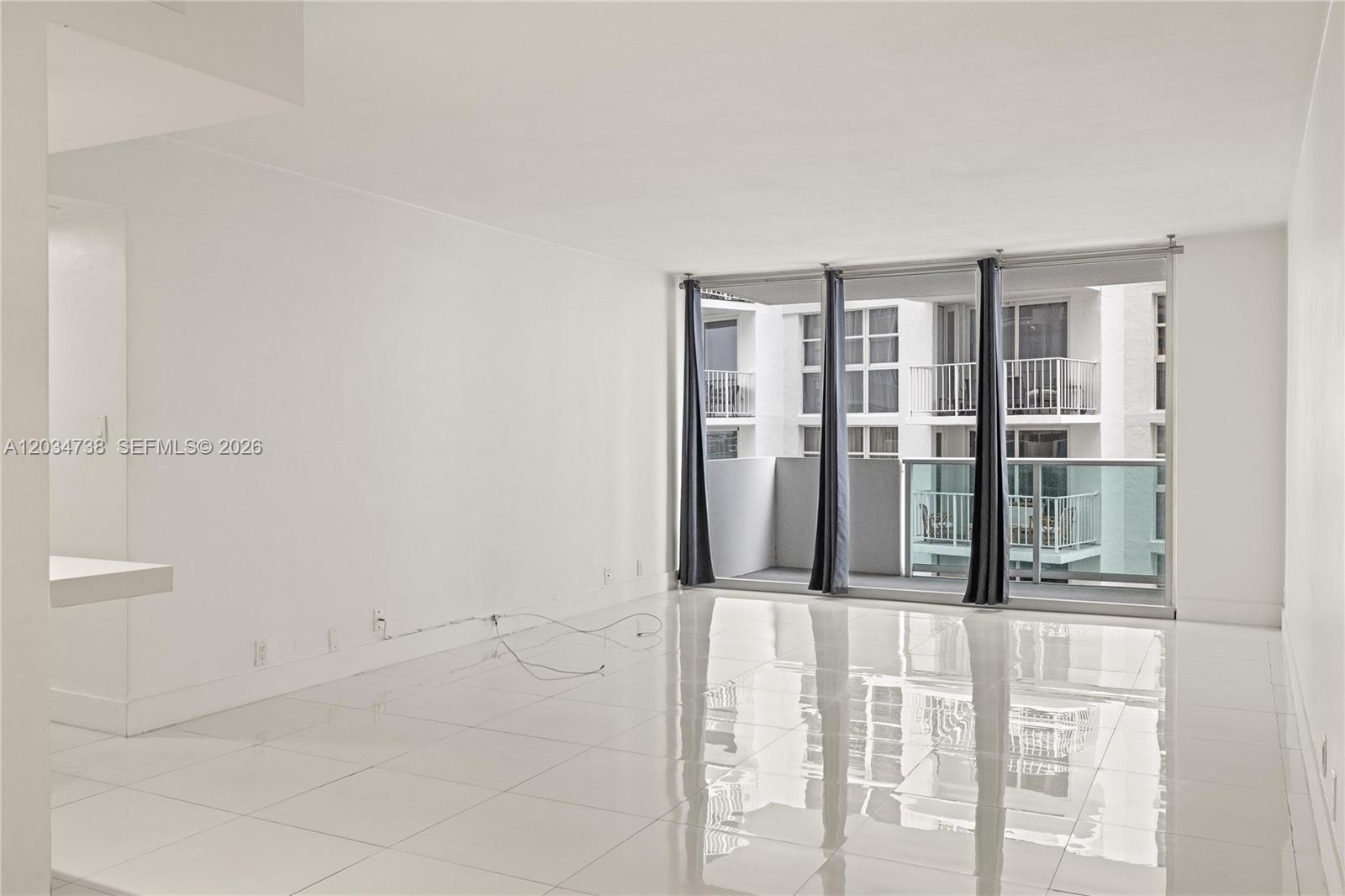 A bright, empty living room features white tile floors, plain walls, and a balcony view — 1200 West Ave # 622, Miami Beach FL 33139, MIAMI BEACH, FL