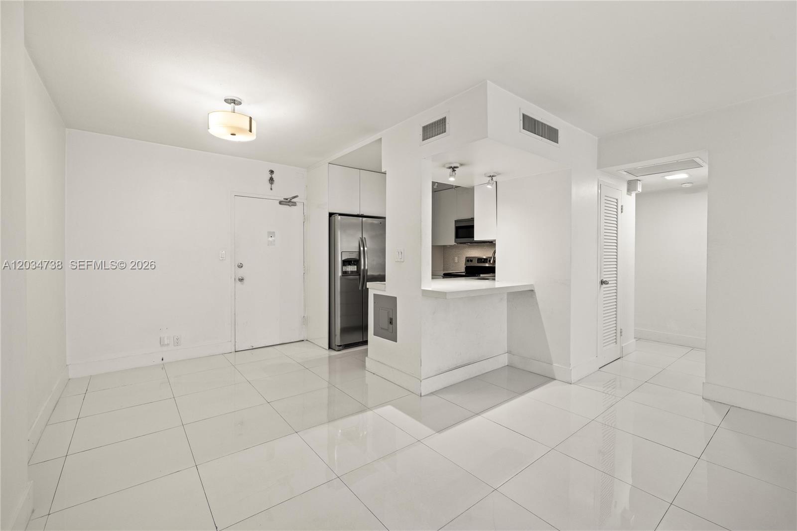 A kitchen with stainless steel appliances and a breakfast bar opens into a tiled room — 1200 West Ave # 622, Miami Beach FL 33139, MIAMI BEACH, FL
