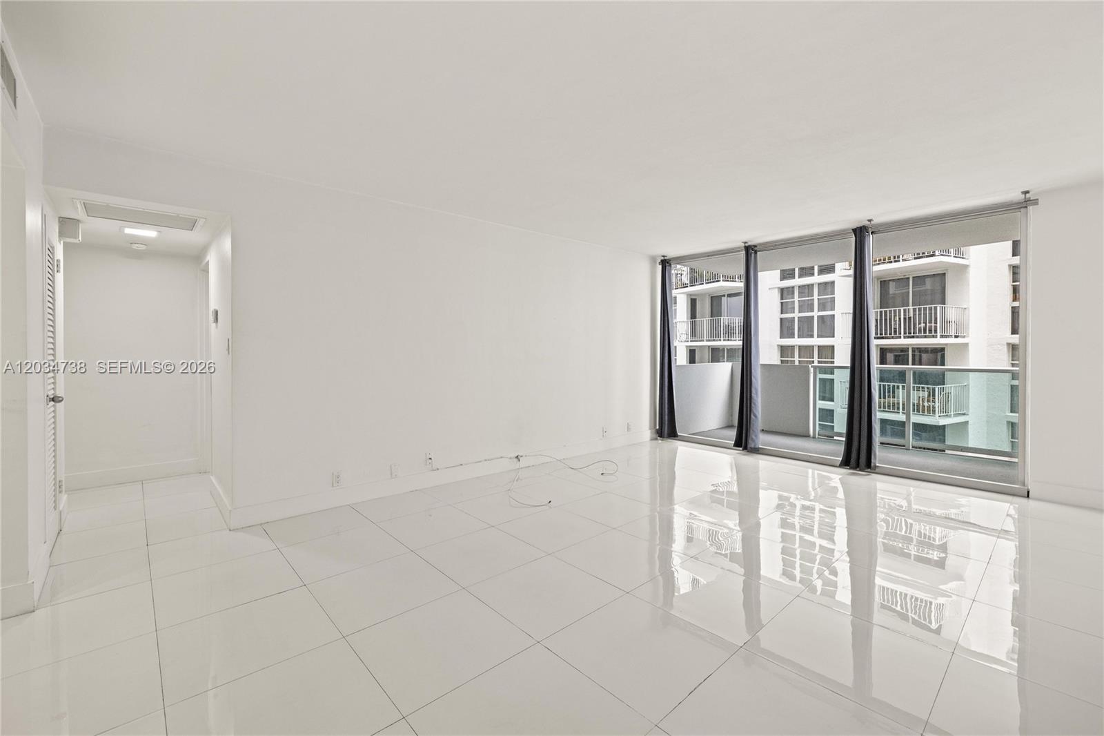 An empty room with white walls, glossy tile floors, and a balcony with glass railings — 1200 West Ave # 622, Miami Beach FL 33139, MIAMI BEACH, FL