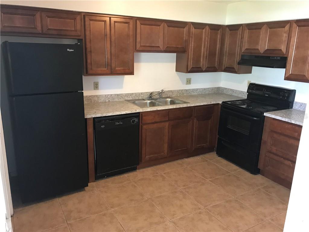A kitchen features dark wood cabinets, black appliances, laminate countertops, and light-colored tile flooring — 2415 S CEDAR AVENUE UNIT B, SANFORD, FL