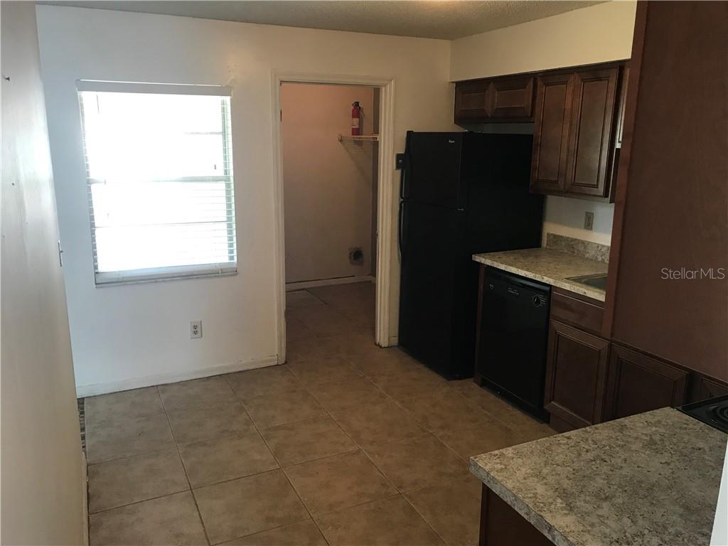 A kitchen features dark wood cabinets, black appliances, tile flooring, and an adjacent utility room — 2415 S CEDAR AVENUE UNIT B, SANFORD, FL