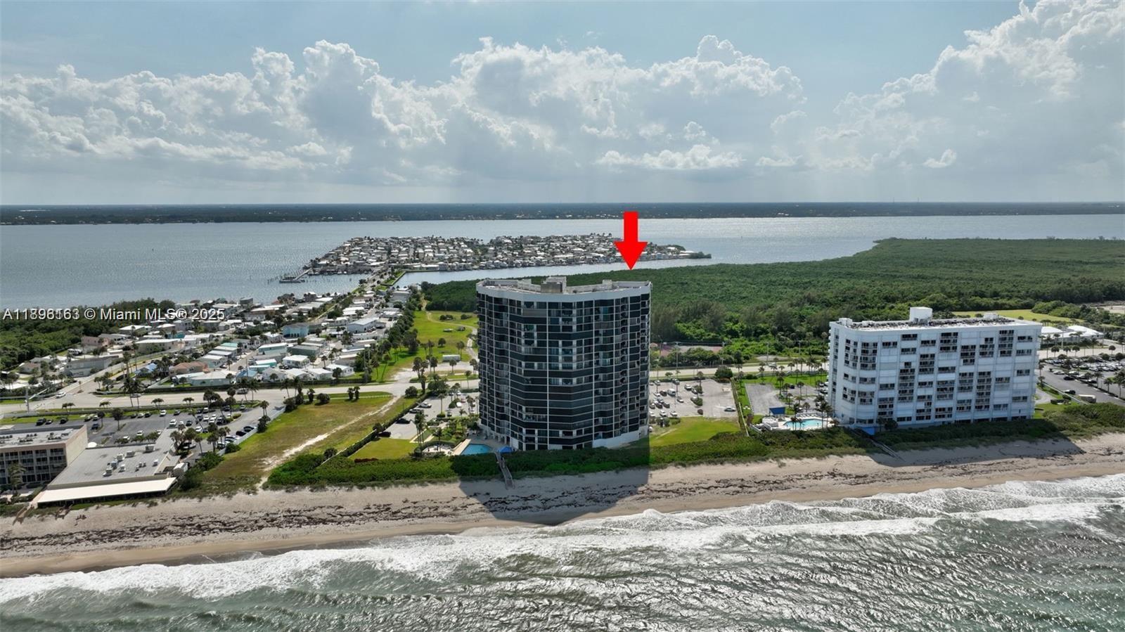 An aerial view shows a tall, dark-colored residential building situated on a sandy beach — 9650 S Ocean Dr # 2003, Jensen Beach FL 34957, JENSEN BEACH, FL