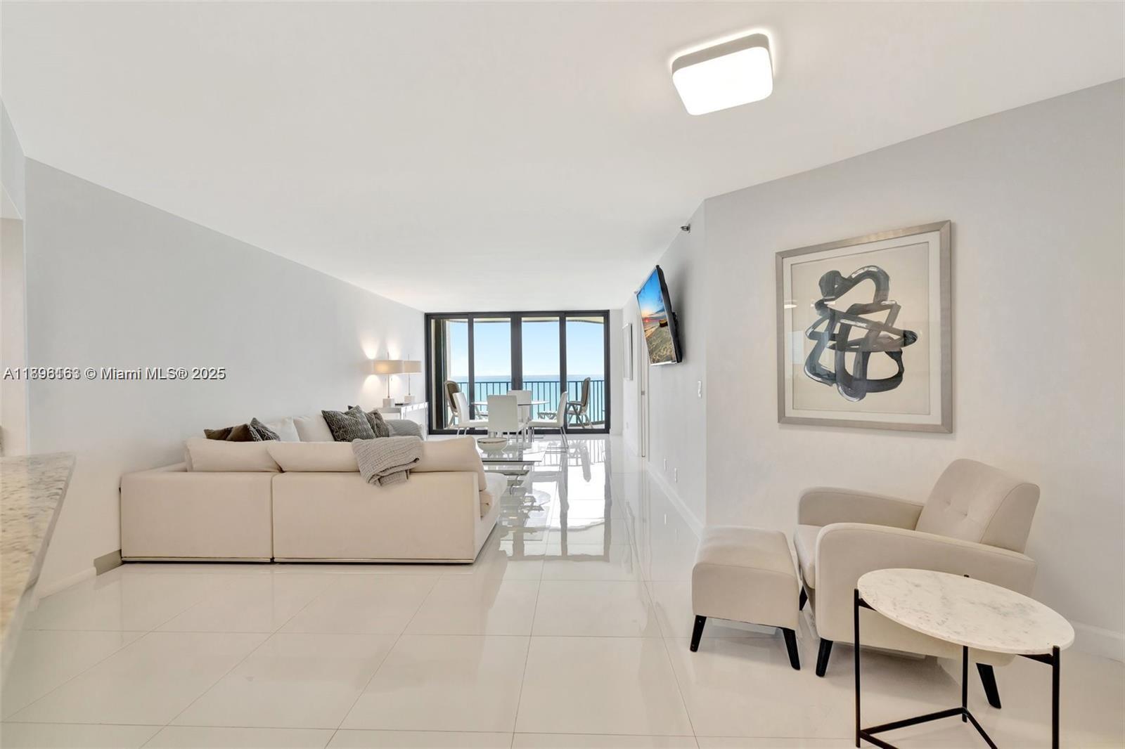 A bright living room features white tile floors, a sectional sofa, and a balcony view — 9650 S Ocean Dr # 2003, Jensen Beach FL 34957, JENSEN BEACH, FL