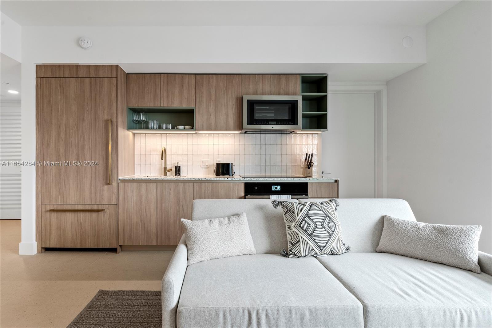 A modern kitchen with wood-toned cabinetry and a white tiled backsplash sits behind a sofa — 601 NE 1st Ave # 2905, Miami FL 33132, MIAMI, FL