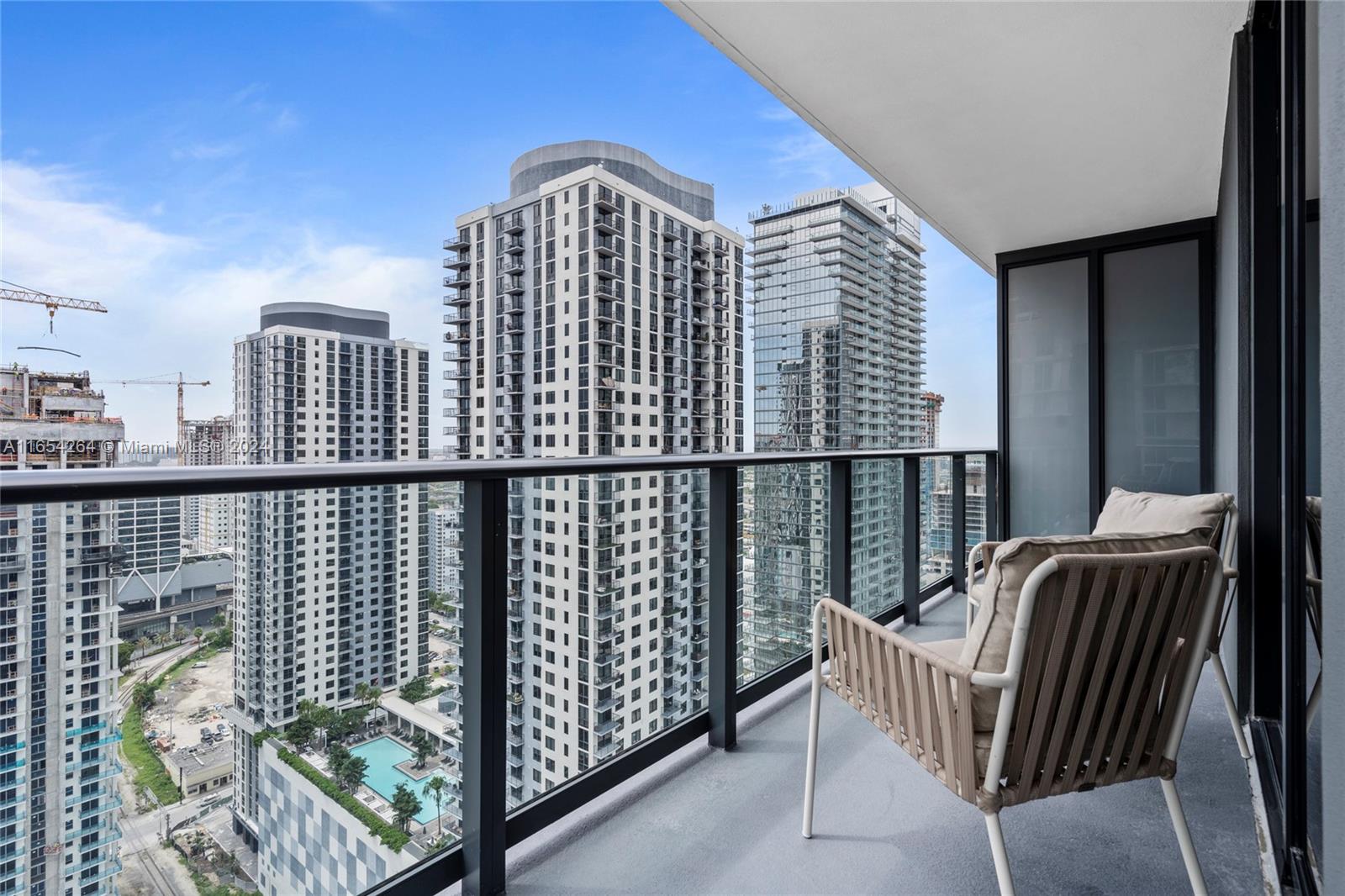 A balcony with a chair overlooks a city skyline featuring several high-rise apartment buildings — 601 NE 1st Ave # 2905, Miami FL 33132, MIAMI, FL