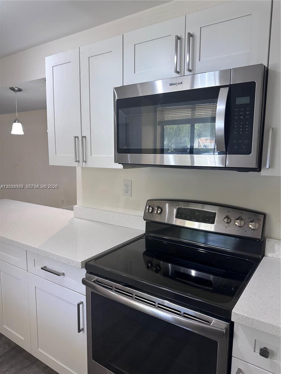 A kitchen features white cabinets, stainless steel appliances, and light-colored quartz countertops — WESTON, FL