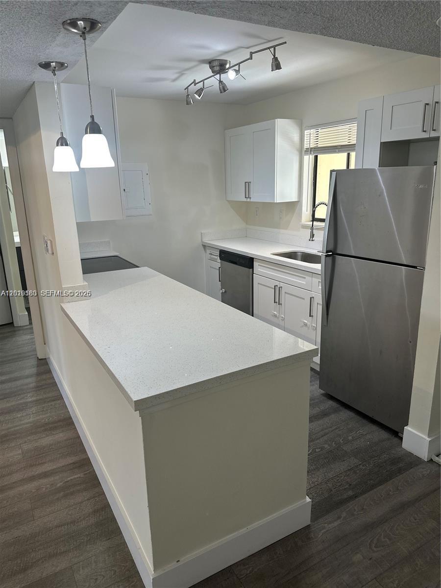 A kitchen features white cabinets, stainless steel appliances, a quartz countertop island, and wood flooring — WESTON, FL