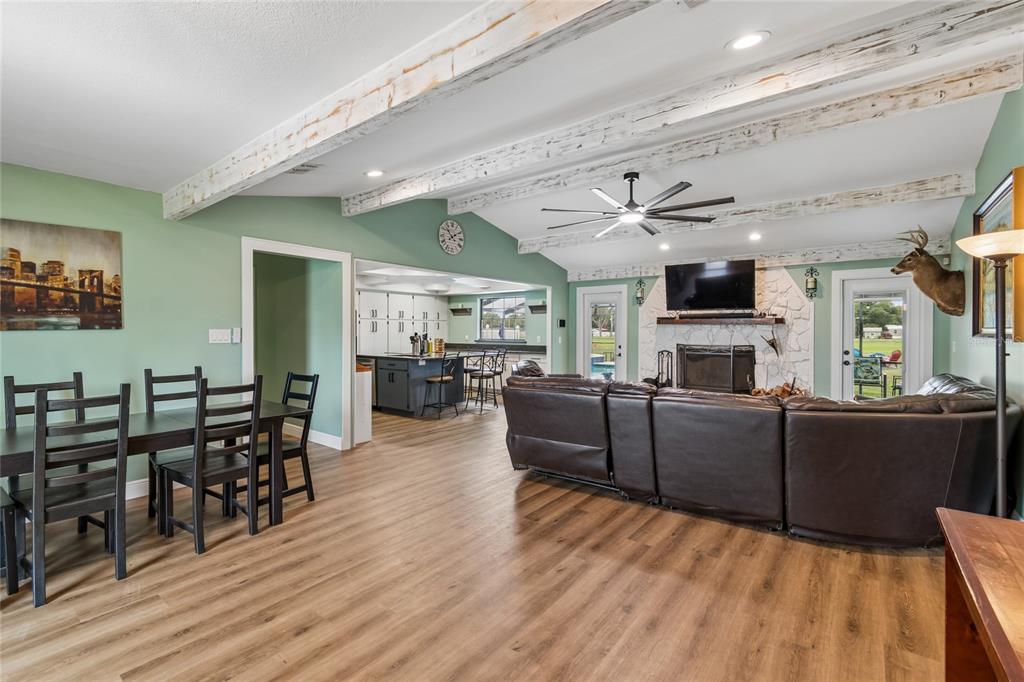 An open-concept living and dining area features wood-look flooring, exposed ceiling beams, and a fireplace — 5150 SOUTHWIND DRIVE, MULBERRY, FL