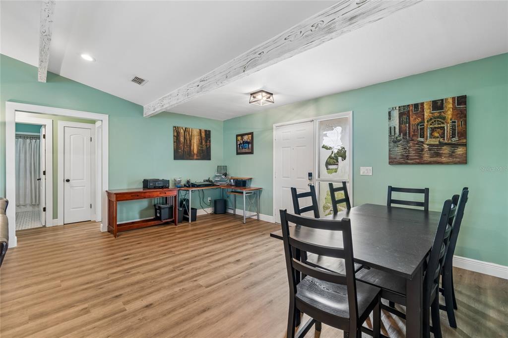 A dining room with light green walls, wood-look flooring, exposed ceiling beams, and a dark table — 5150 SOUTHWIND DRIVE, MULBERRY, FL