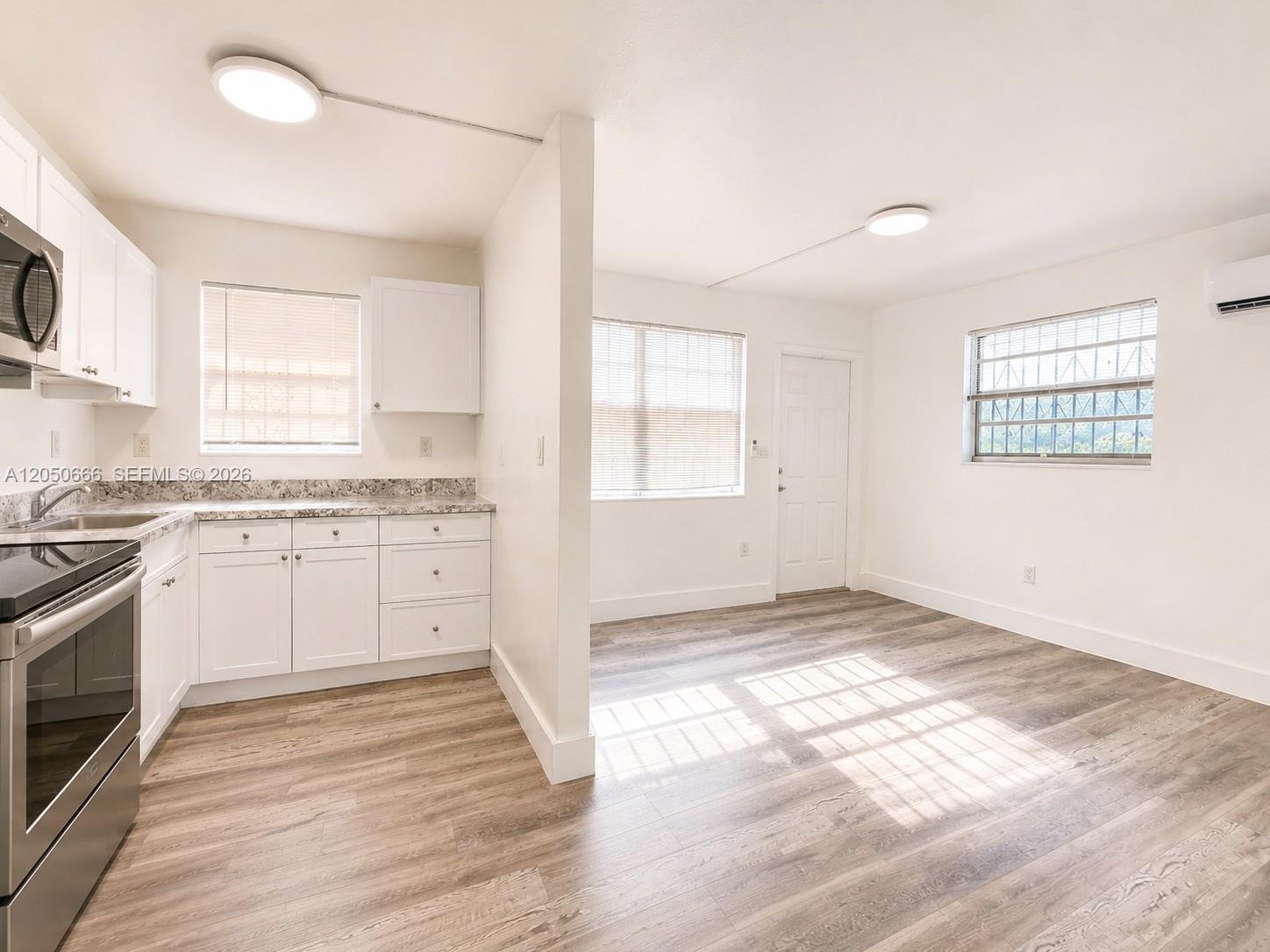 A kitchen with white cabinets and stainless steel appliances opens into a living area — 46 NW 62nd St # 4, Miami FL 33150, MIAMI, FL