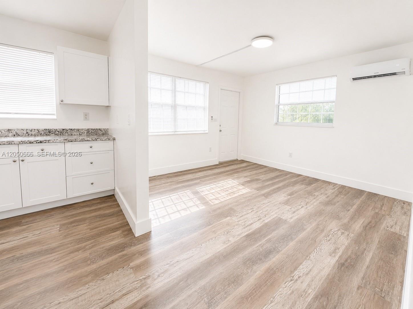 A bright room features white cabinets, granite countertops, light wood-look flooring, and a wall-mounted air conditioner — 46 NW 62nd St # 4, Miami FL 33150, MIAMI, FL