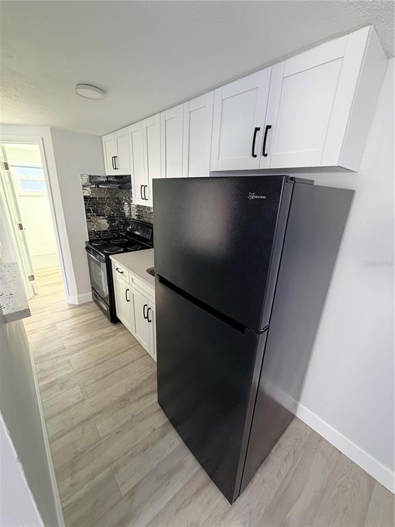 A kitchen features white cabinets, a black refrigerator, a black stove, and light wood flooring — 1101 E 140TH AVENUE, TAMPA, FL