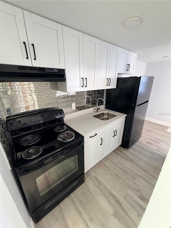 A kitchen features white cabinets, a black stove, a black refrigerator, and a tiled backsplash — 1101 E 140TH AVENUE, TAMPA, FL
