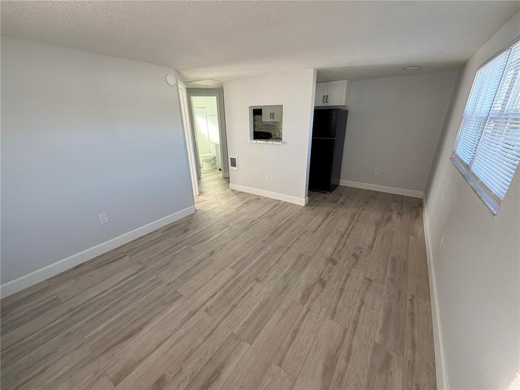 A living area with light wood-look flooring, a pass-through window, and a black refrigerator — 1101 E 140TH AVENUE, TAMPA, FL