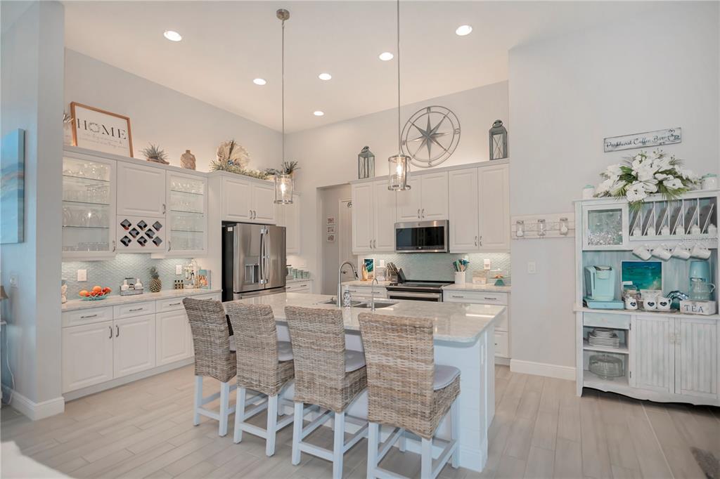 A bright kitchen features white cabinetry, a large island with wicker stools, and stainless appliances — 10136 AMY TERRACE, PORT CHARLOTTE, FL