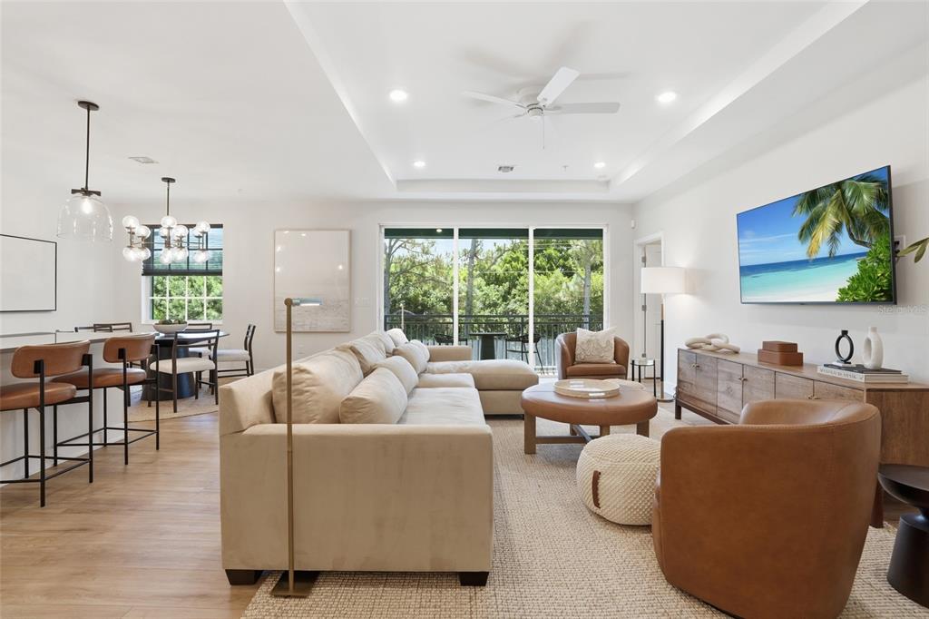 A modern open-concept living and dining area features neutral furniture, wood flooring, and large windows — 26380 COCO CAY CIRCLE UNIT 202, BONITA SPRINGS, FL