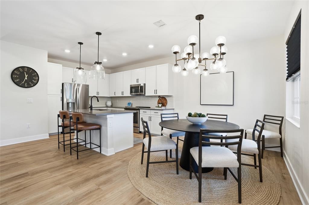 A modern kitchen and dining area features white cabinets, stainless appliances, and a round table — 26380 COCO CAY CIRCLE UNIT 202, BONITA SPRINGS, FL