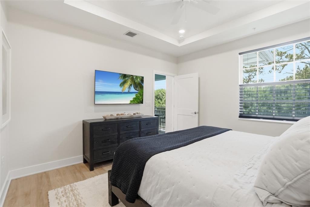 A bedroom features a dark wood dresser, a wall-mounted television, and a white bed — 26380 COCO CAY CIRCLE UNIT 202, BONITA SPRINGS, FL