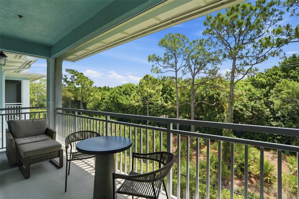 A covered balcony features a small table, two chairs, and a lounge chair overlooking trees — 26380 COCO CAY CIRCLE UNIT 202, BONITA SPRINGS, FL