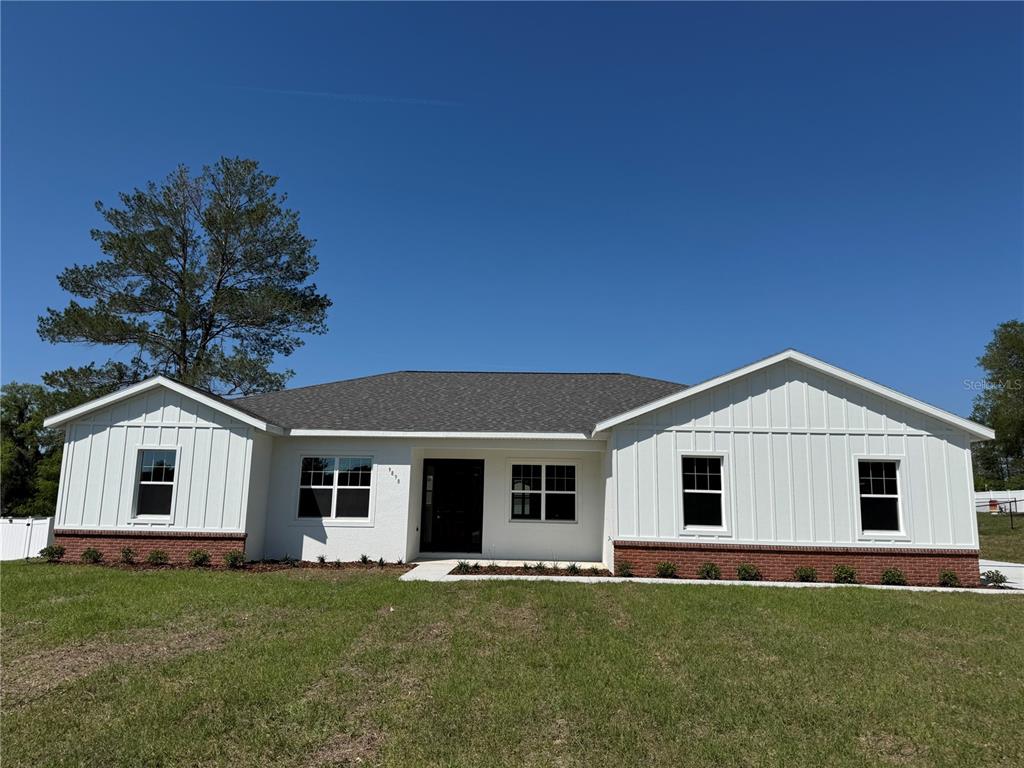 A single-story house with white board-and-batten siding, brick accents, and a dark shingled roof — 4198 SW 112TH STREET, OCALA, FL