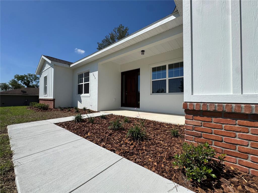 A white house exterior features a brick base, a covered entryway, and a concrete walkway — 4198 SW 112TH STREET, OCALA, FL
