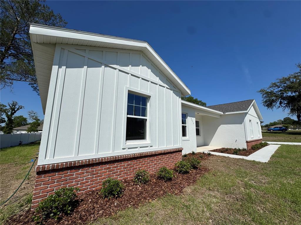 A white board-and-batten house exterior features a brick base and a small front porch — 4198 SW 112TH STREET, OCALA, FL
