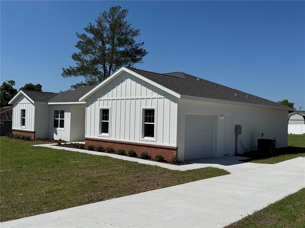 A single-story house with white board-and-batten siding, a brick base, and a concrete driveway — 4198 SW 112TH STREET, OCALA, FL