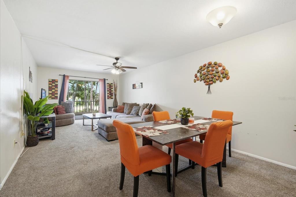 A living and dining area features carpeted floors, orange chairs, and a sliding glass door — 7500 40TH AVENUE W UNIT 203, BRADENTON, FL