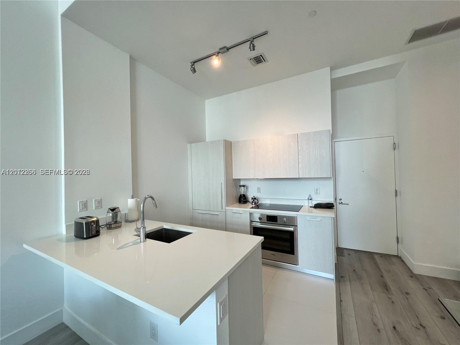 A modern kitchen features white cabinetry, a quartz island with a sink, and stainless appliances — 501 NE 31st St # 404, Miami FL 33137, MIAMI, FL
